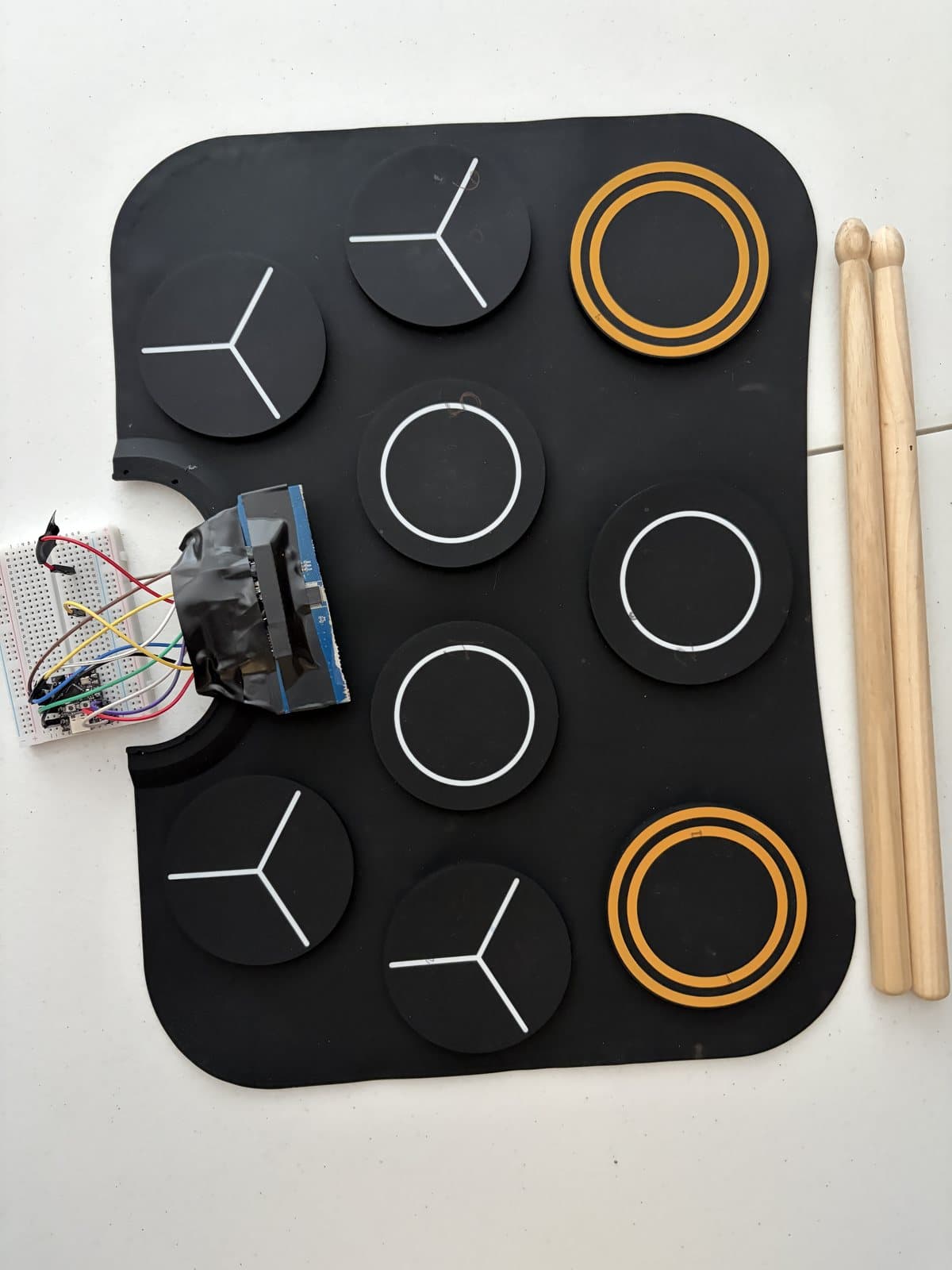 Drum Cockpit from above: a nine-pad drum mat wired to an ESP32 board on a breadboard, with drumsticks beside it.