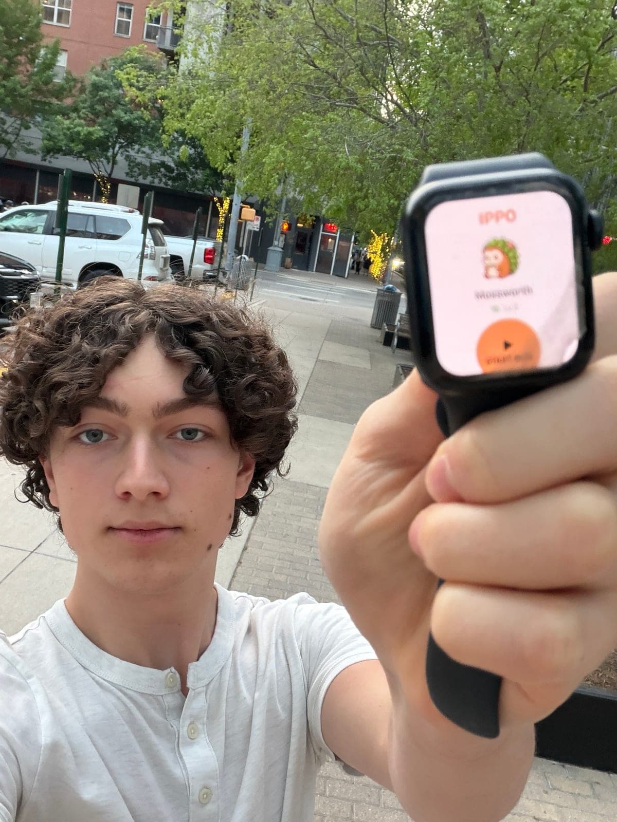 Cruce on a downtown Austin sidewalk holding his Apple Watch up to the camera, the Ippo app on its screen.
