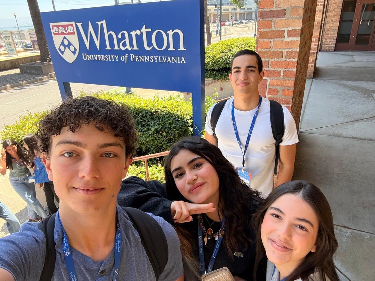 Cruce taking a selfie with three Wharton Global Youth classmates in front of the blue Wharton, University of Pennsylvania sign at the San Francisco campus.
